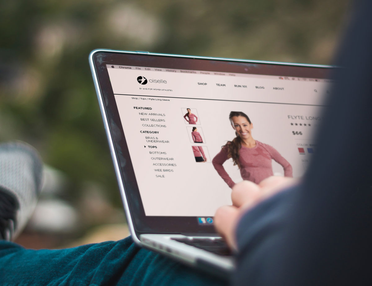 A mockup of an outdoorsy person sitting on the ground browsing the Oiselle website.